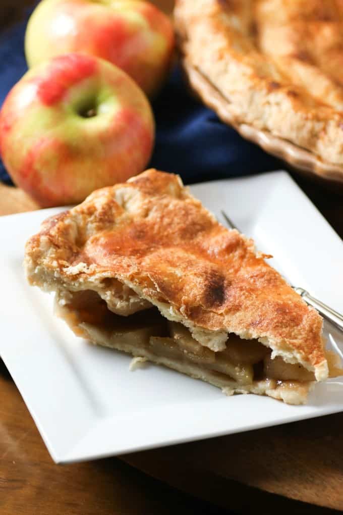 Learn all the tips and tricks you need on How To Make The Perfect Pie Crust!! #pie #piecrust #potpie Slice of apple pie on a white plate with apples in the background