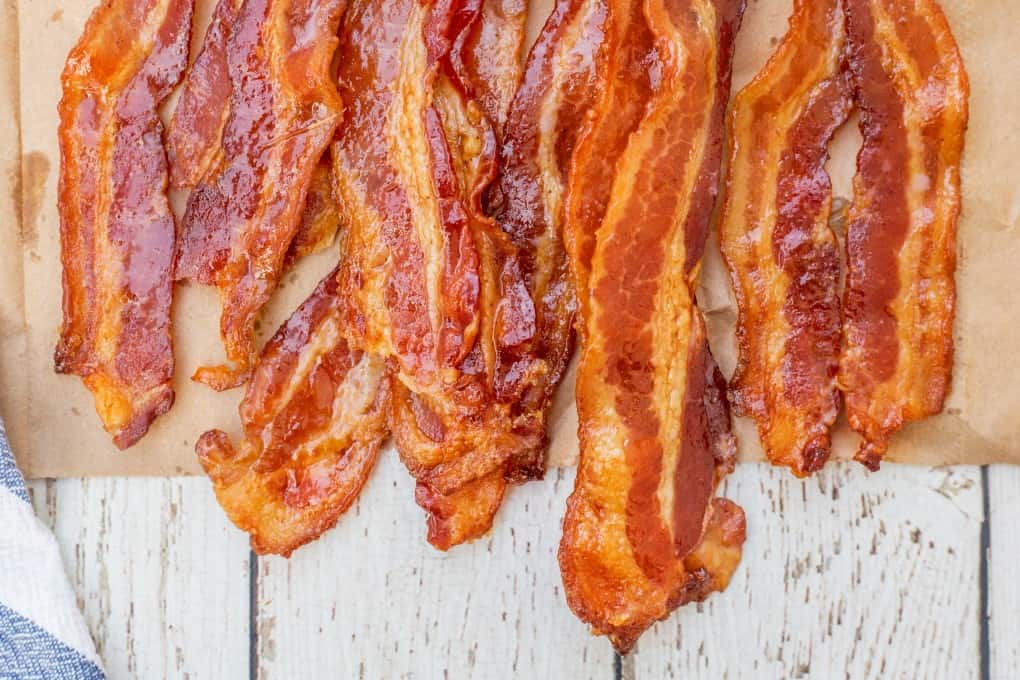 This amazing Brown Sugar Bacon will amp up your breakfast or brunch to a whole new level. We love the spicy sweetness! #brownsugarbacon #sweetandspicybacon Close up of crispy cooked bacon on a paper bag