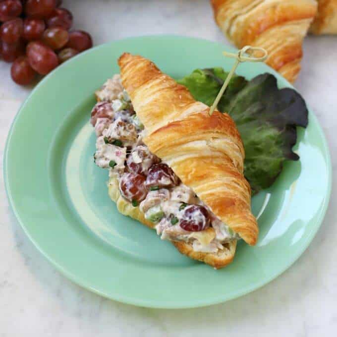This simple recipe for Chicken Salad with Grapes can't be beat for a delicious easy salad for sandwiches or on its own. Enjoy a great combination of chicken, grapes, and celery to make a refreshing meal. #chickensalad #grapes #sandwiches A green plate containing a croissant filled with chicken salad