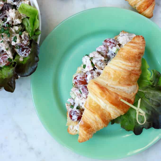 This simple recipe for Chicken Salad with Grapes can't be beat for a delicious easy salad for sandwiches or on its own. Enjoy a great combination of chicken, grapes, and celery to make a refreshing meal. #chickensalad #grapes #sandwiches An overhead shot of a green plate containing a croissant filled with chicken salad