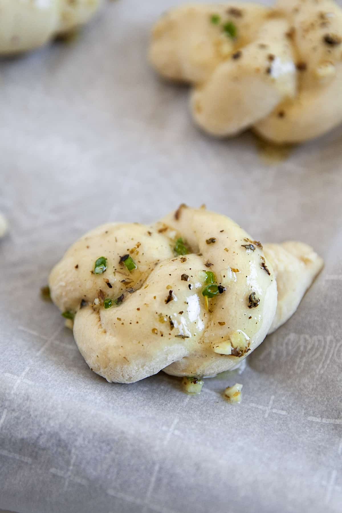 Once you have these garlic knots, you will want to make them again and again. They are great as an appetizer but work amazing as a side dish for dunking into soups, stews, pasta and so much more. Garlic knots with butter on them ready for the oven. Close-up of one.