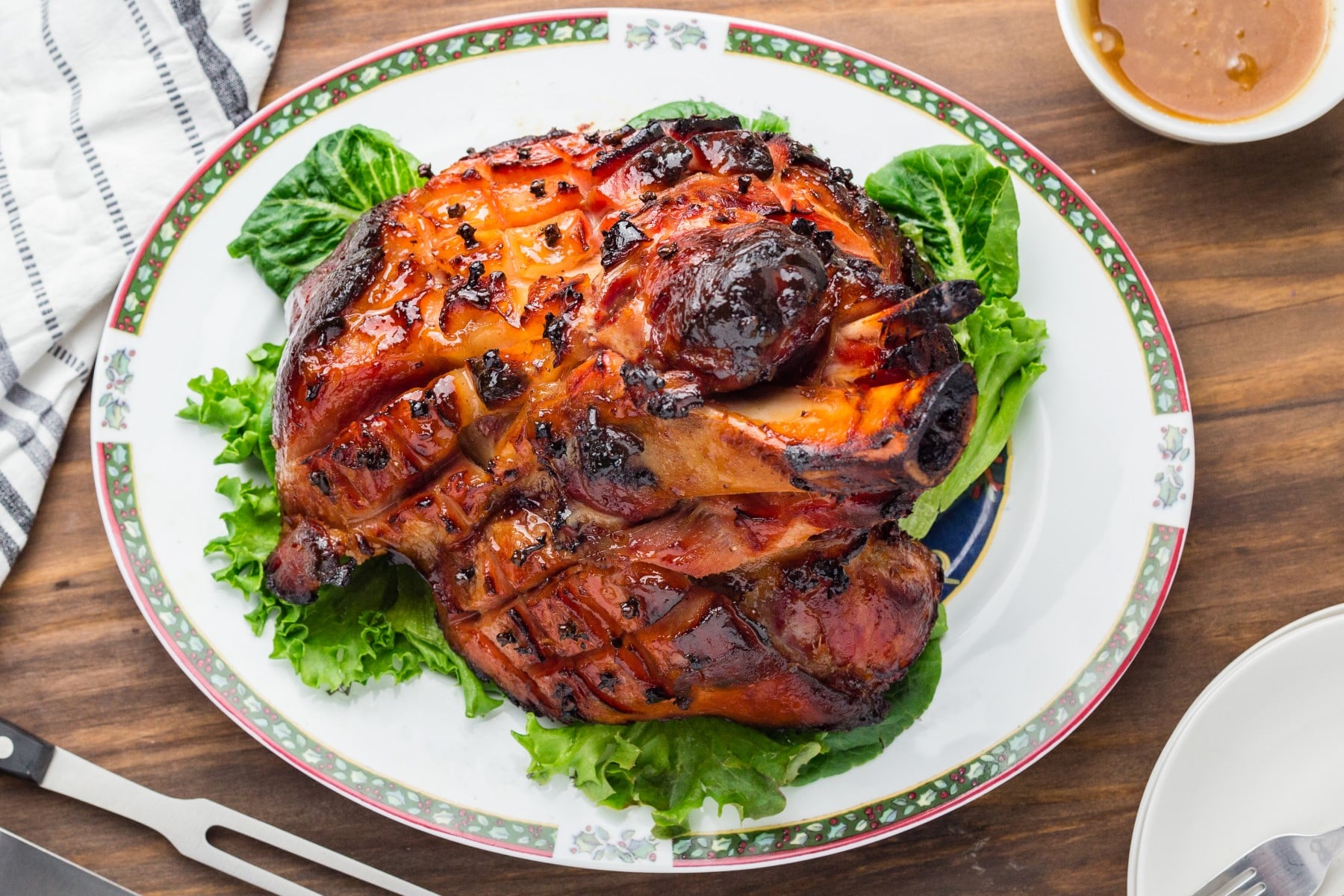 Learn How to Cook a Ham with this informative post, plus an amazing glaze to keep the ham moist and delicious. Horizontal shot of ham on a plate over lettuce.