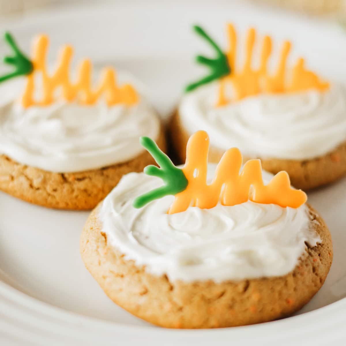These Carrot Cake Cookies couldn't be easier with a mix and canned icing. All you need to do is a little candy carrot, and you have the most adorable cookie around. Carrot Cake Cookies close-up on a plate.