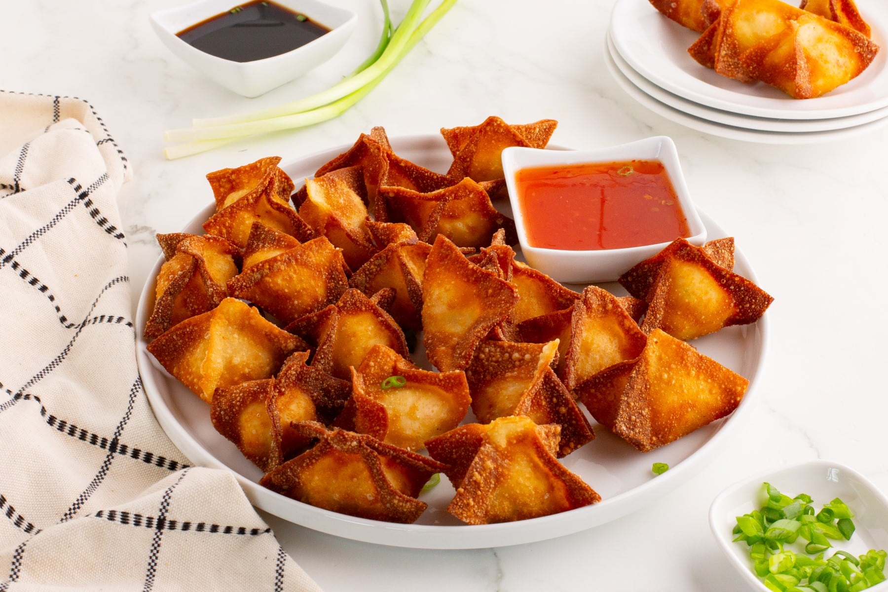 This Crab Rangoon recipe will change how you think of takeout when you can make these easy and fun appetizers at home. Fresh out of the oil and crispy, it is so delicious. Crab rangoon served on a white platter with a bowl of dipping sauce.